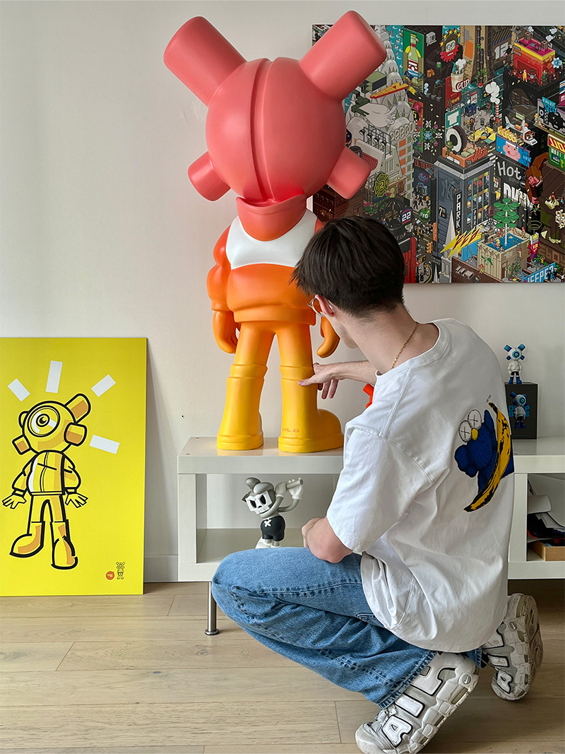 Une sculpture EQSO de 120 cm en dégradé rose, orange et jaune, posée sur un meuble, vue de dos