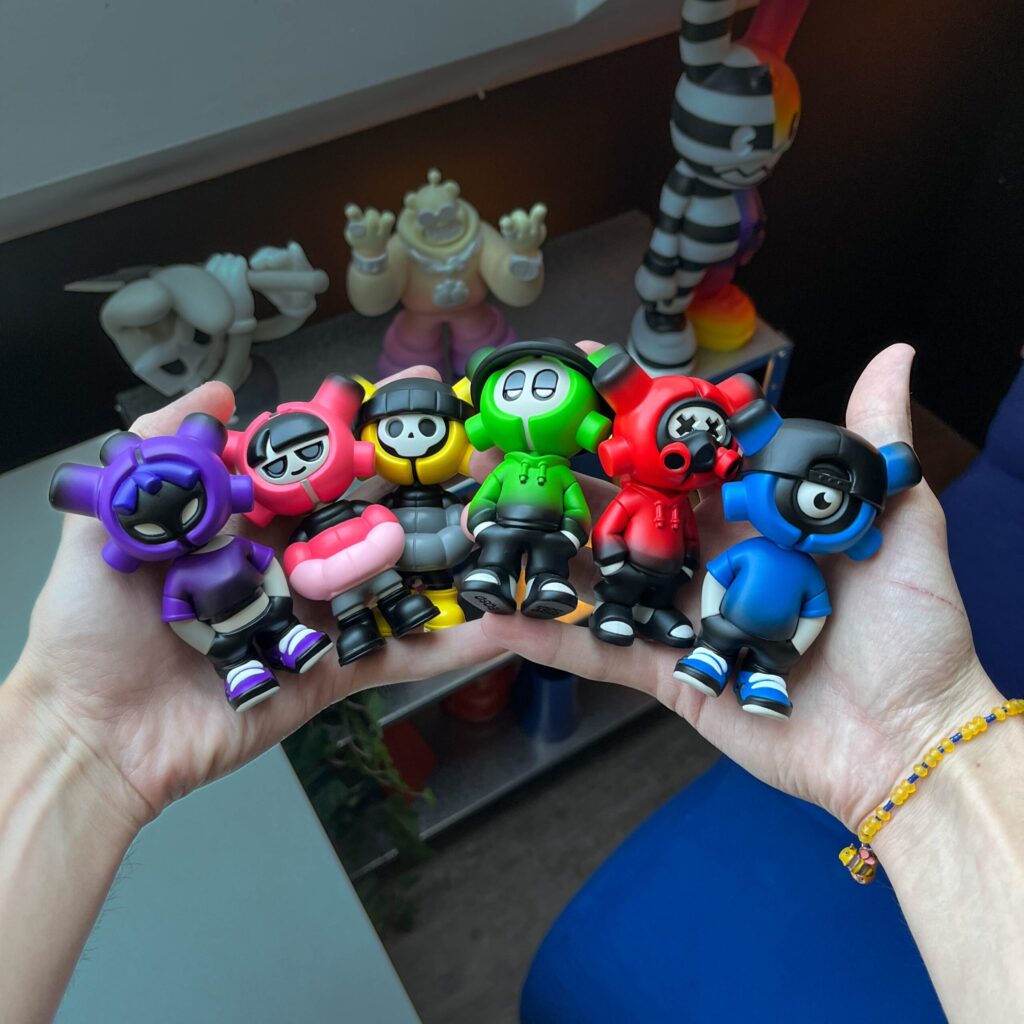 Les six figurines de la blind box EQSO The Crew tenues dans deux mains : Purple, Cherry, Skully, Supagreen, Vandal et Cyclo